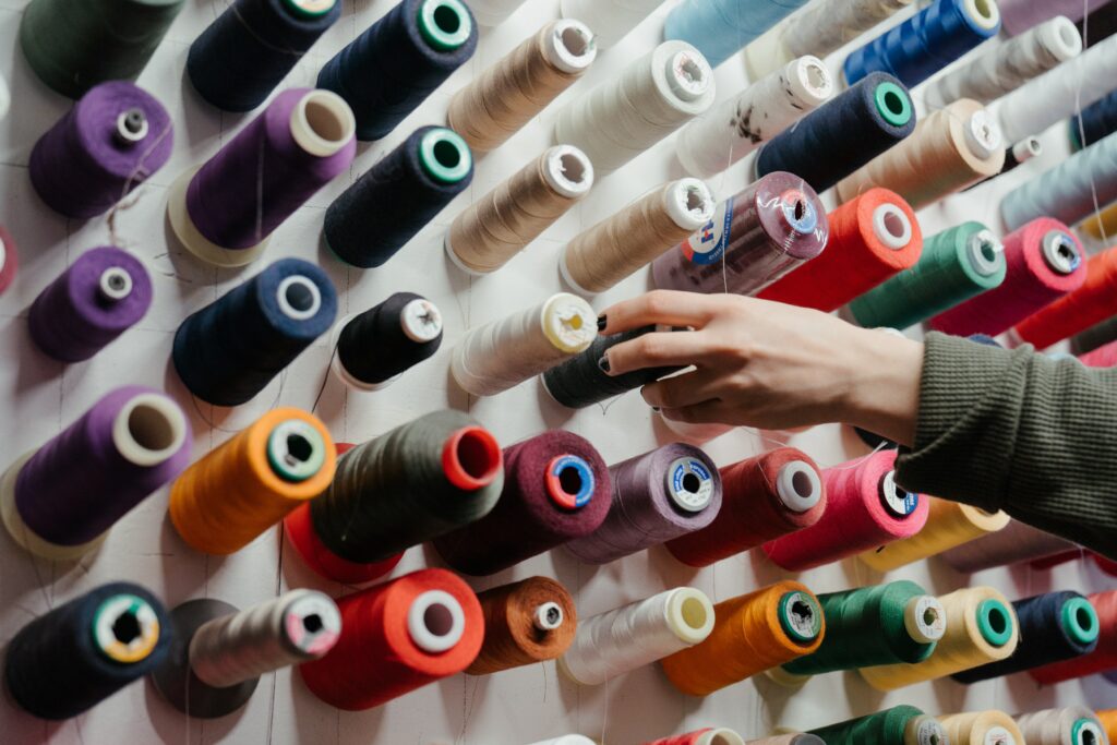 A hand reaching to choose one spool of thread, among many different spools of colored thread.